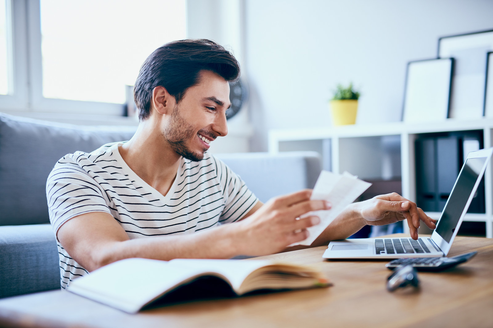 Man holding paper receipts and typing on a laptop