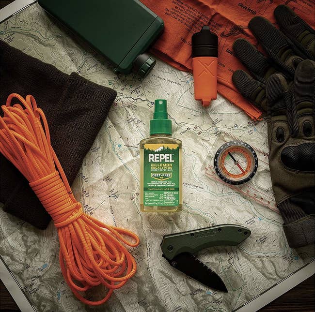 the spray on a map surrounded by other camping supplies like a compass and pocket knife
