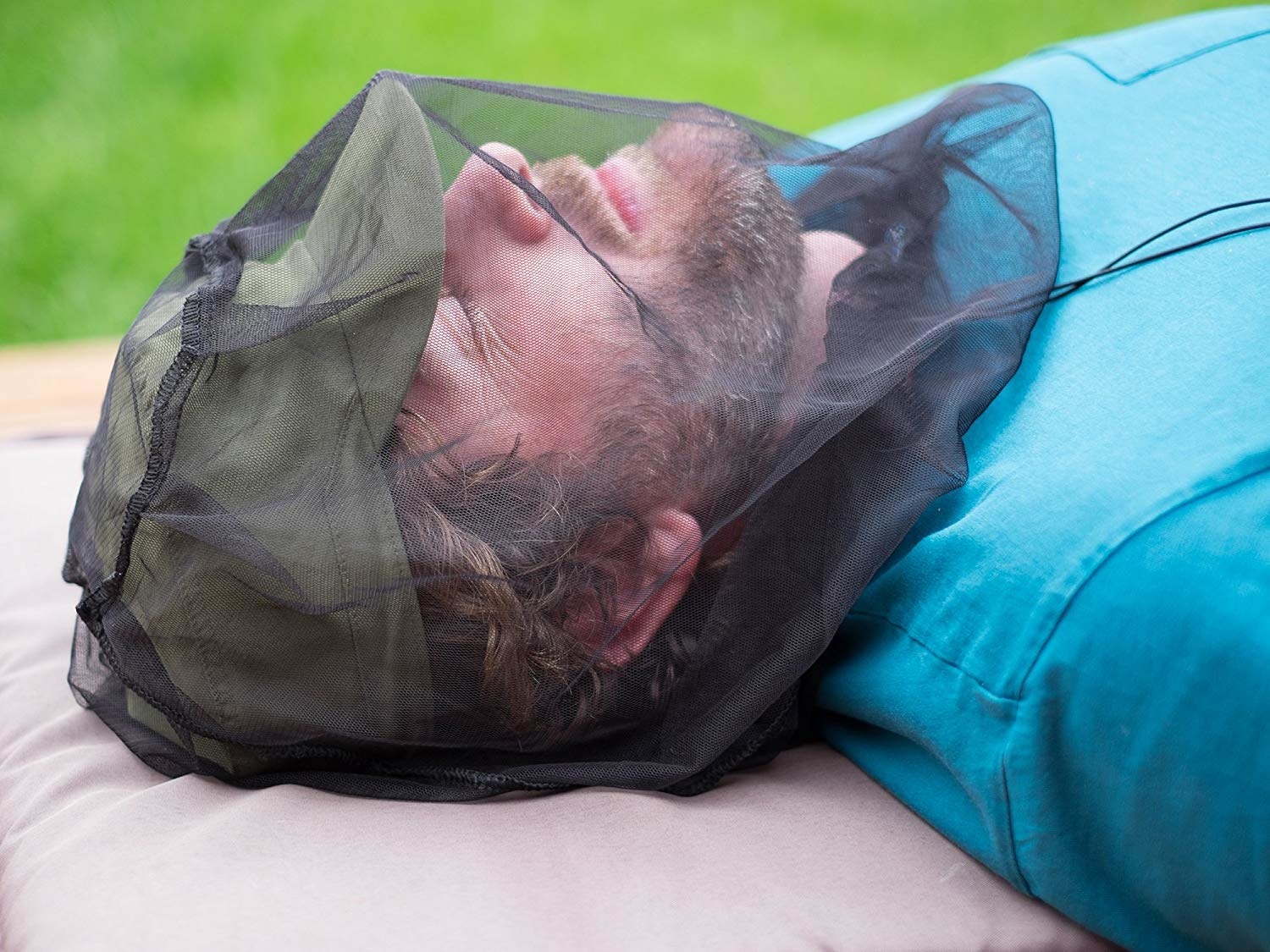 person laying down outside with the net over a baseball cap