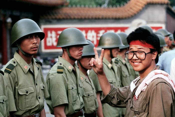 A pro-democracy demonstrator gives the &quot;V for Victory&quot; sign to soldiers who are lined up, standing guard outside the Chinese Communist Party&#x27;s headquarters.