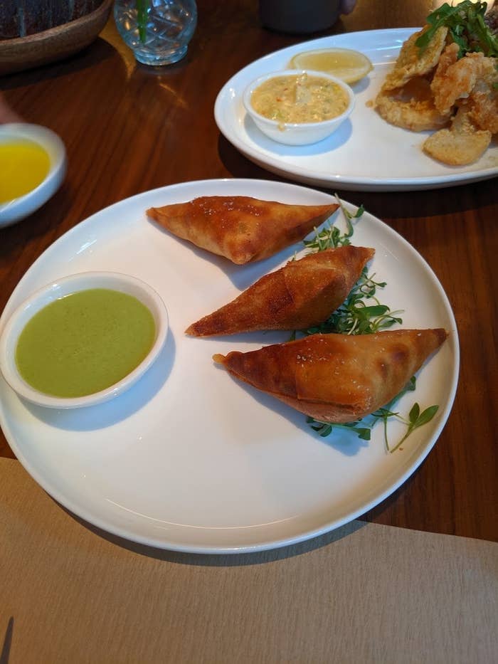 Three pieces of samosas are filled with savory chicken, and served with a side of cilantro-yogurt dipping sauce. The samosas are crispy without being too greasy.