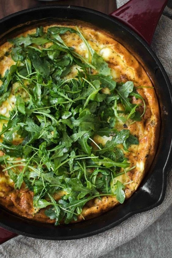 Close-up of a skillet frittata topped with fresh arugula. The edges are crispy and slightly browned, indicating it&#x27;s freshly cooked and ready to be served
