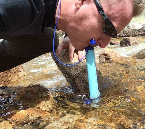 A reviewer drinking out of a lake with the Lifestraw 