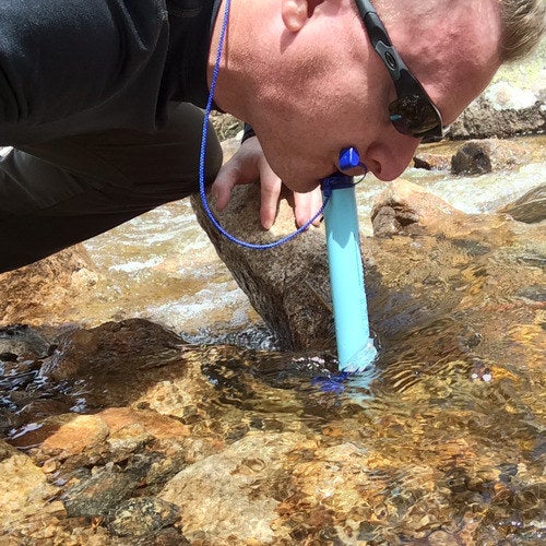 A reviewer drinking out of a lake with the Lifestraw 