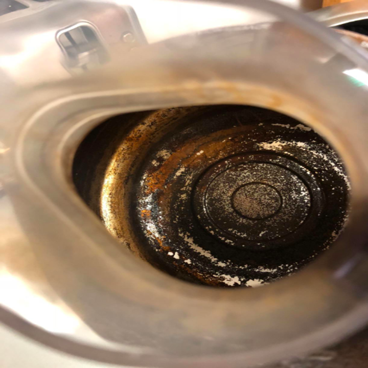 before: bottom of a stainless steel coffee put caked with black and brown burned on old coffee