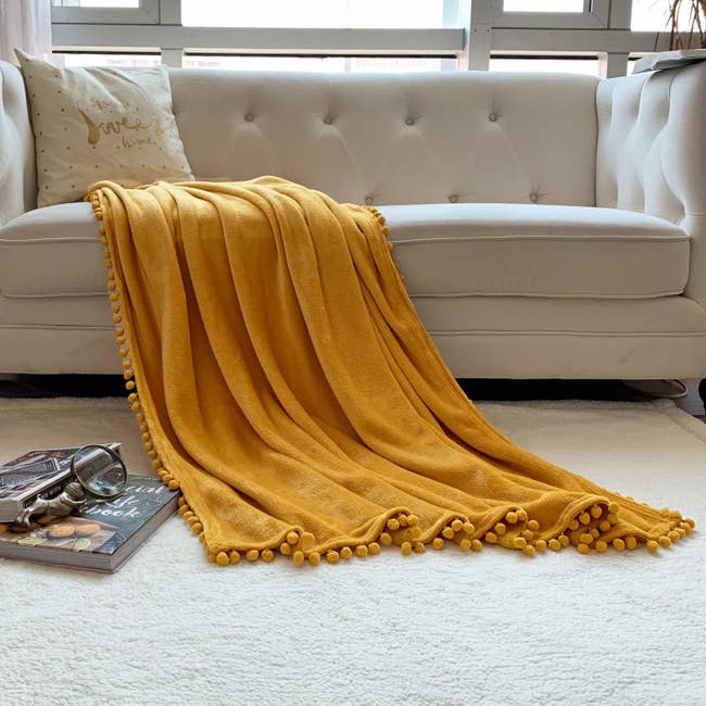 yellow blanket with pom pom trim on it thrown over a beige couch