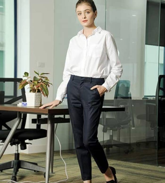 model wearing the ankle dress pants in black and white blouse, standing in an office