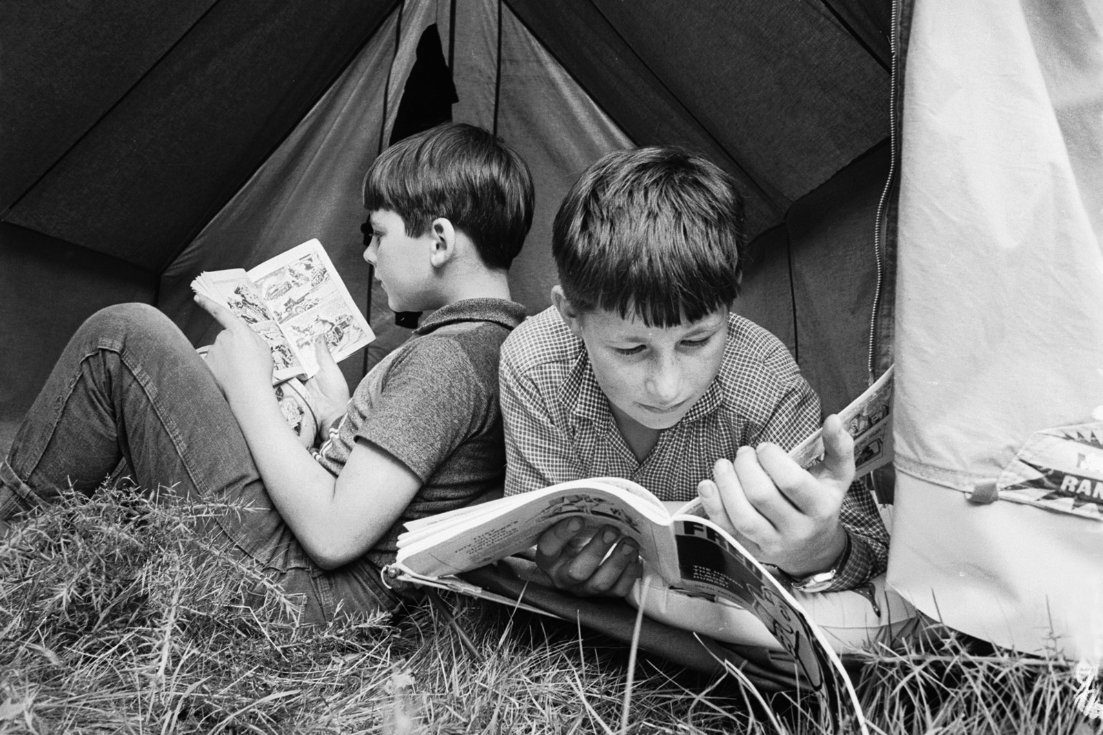A pair of boys read comic books in their tent at a summer camp hosted by th...