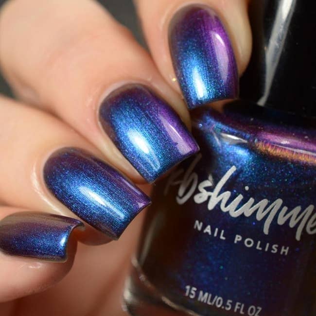 Nails painted in a shimmer metallic blue holding the nail polish bottle