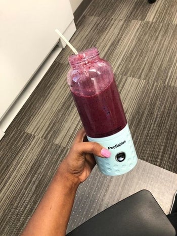 Same hand holding the blender but with a now fully blended smoothie