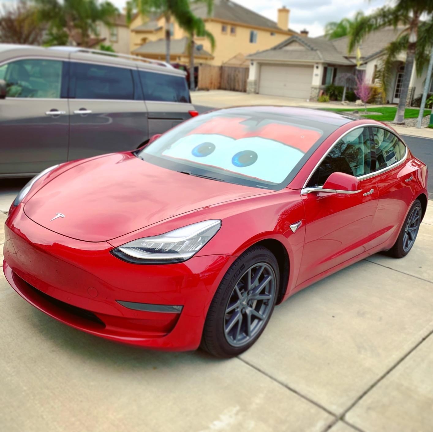 A reviewer&#x27;s red car with the Lightning McQueen eyes shade in the windshield 