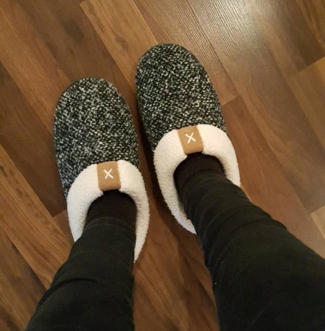 reviewer wearing the slippers, which have a white sherpa lining and a black and white speckle pattern