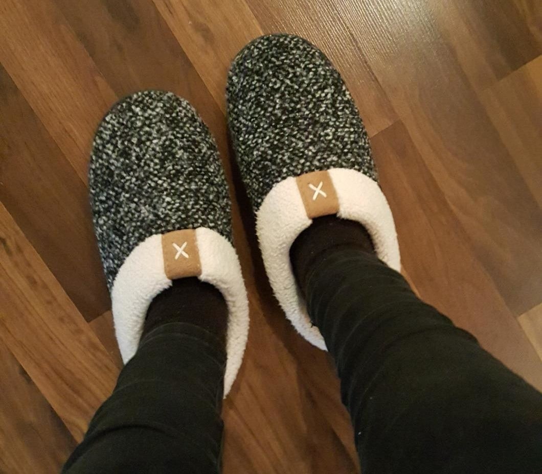 reviewer wearing the slippers which have a white and black speckle pattern and a white sherpa lining