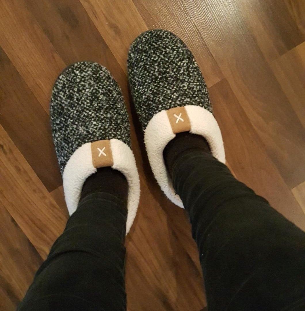reviewer wearing the slippers, which have a white sherpa lining and a black and white speckle pattern