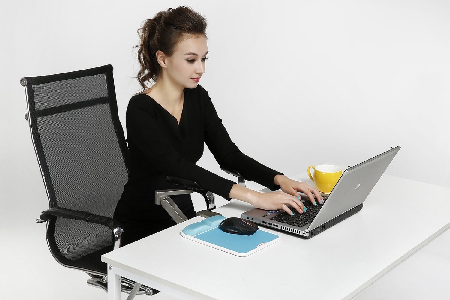 A model types on their laptop, which is sitting on a table, with their arms resting on the armrests