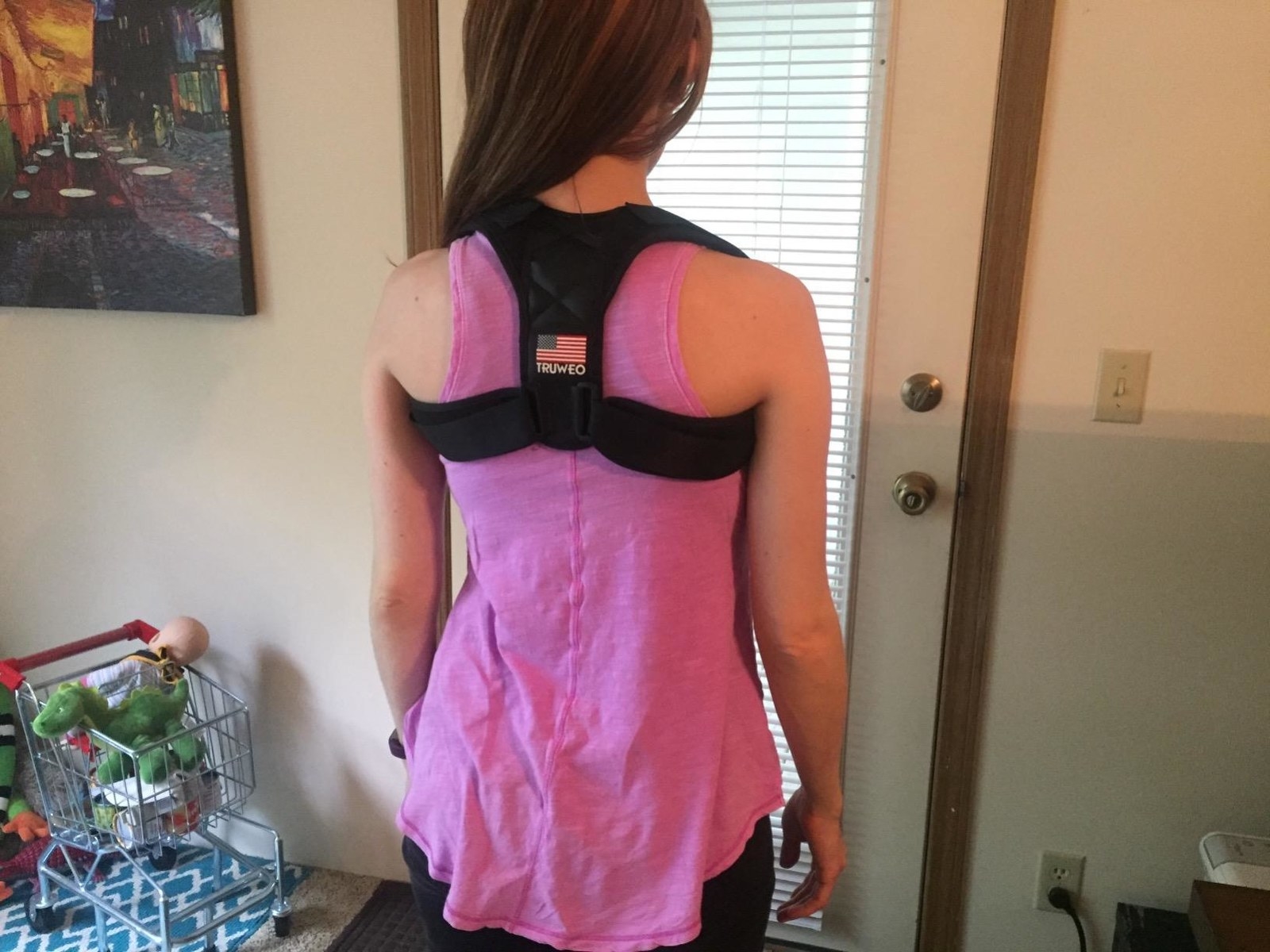 A reviewer wearing the black corrector, which loops around each shoulder, over a tank top
