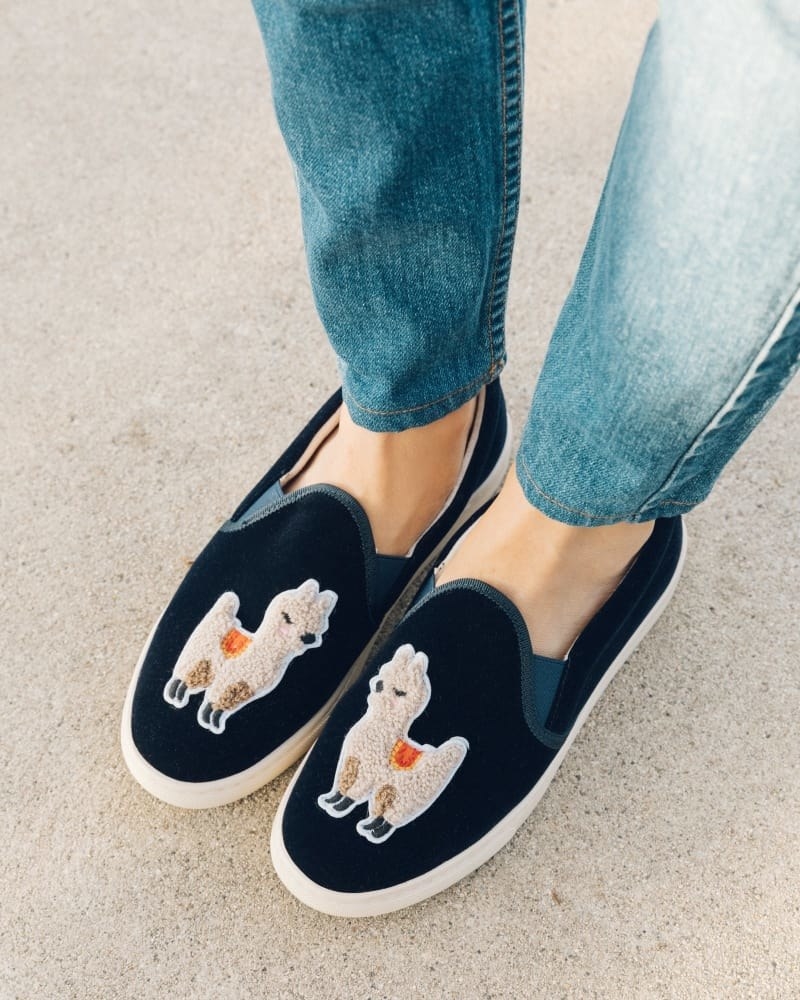 Blue velvet slip-on sneakers with elastic in the corners of the top with a fuzzy llama on top of each one