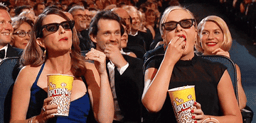 Tina Fey and Amy Poehler eating popcorn and pretending to watch a movie