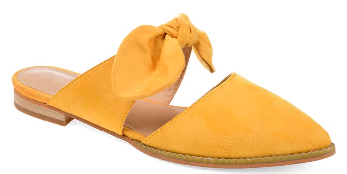 A yellow slip-on, closed toe flat with an accent bow on the strap