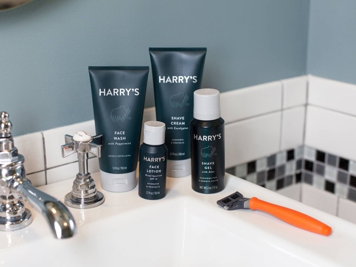 a bottle of Harry&#x27;s face wash, lotion, shave gel, shave cream, and a razor in a bathroom