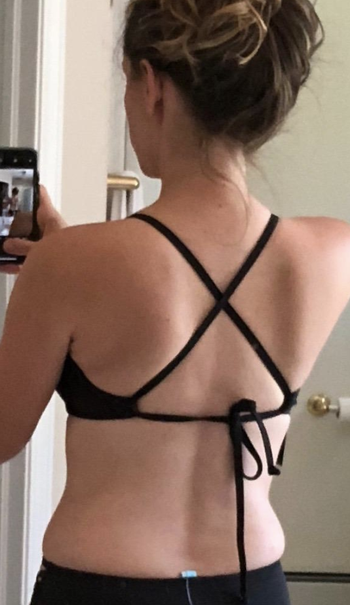 a reviewer showing the criss cross tied back of the black bathing suit top