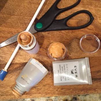 A reviewer's cut-open foundation bottle, tiny spatula with a long handle, and the small jar full of foundation they were able to save