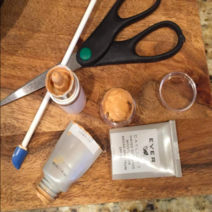 A reviewer's cut-open foundation bottle, tiny spatula with a long handle, and the small jar full of foundation they were able to save