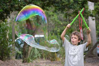 a child holding two wands in the air making a big bubble