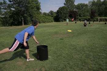 a person lunging over a black kan jam tube while throwing a yellow frisbee to someone across from them in a grassy field