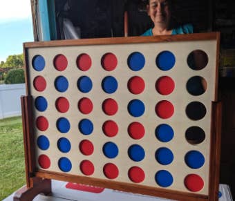 a wooden oversized connect four board game with the open circles filled with either red or blue tokens