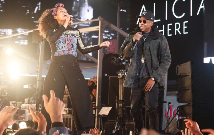 Jay-Z looks at Alicia to his right who is on stage belting
