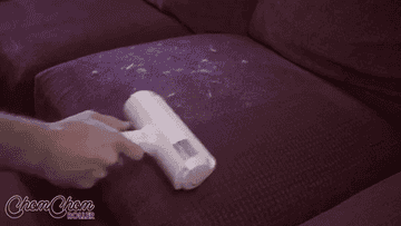 Gif of person removing white fur off a maroon couch using the sticky roller, which has a handle