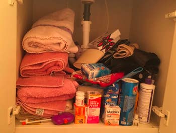 reviewer pic of underneath a bathroom vanity in a cabinet with a jumbled mess of washcloths and toiletries