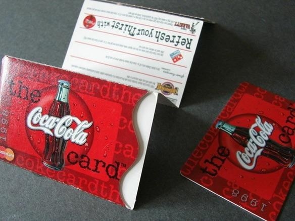 A close of a Coca-Cola Rewards card and the cardboard envelope for it.