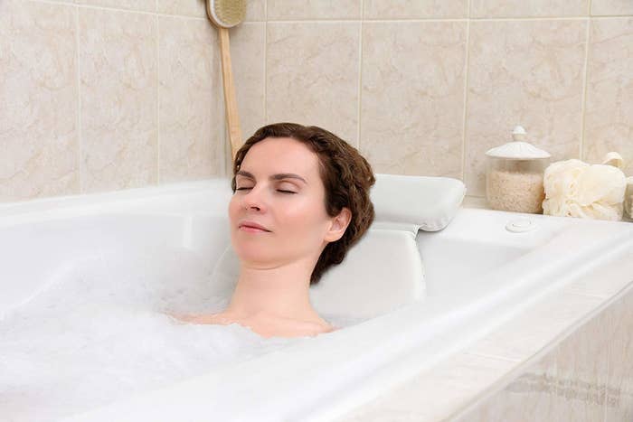 Model resting their head on the bath pillow while in a bubble bath
