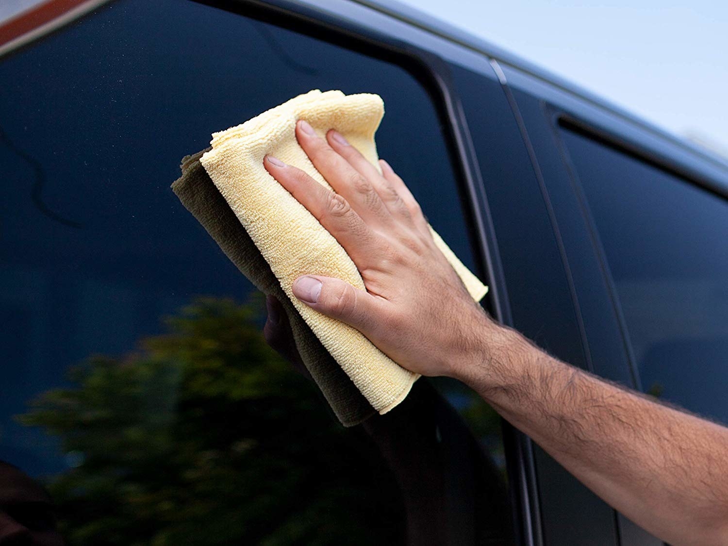 a model using the yellow microfiber towel on a car window
