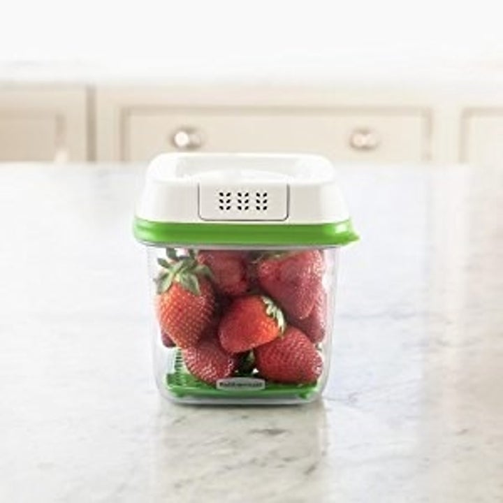The small plastic container filled with strawberries sitting on a counter