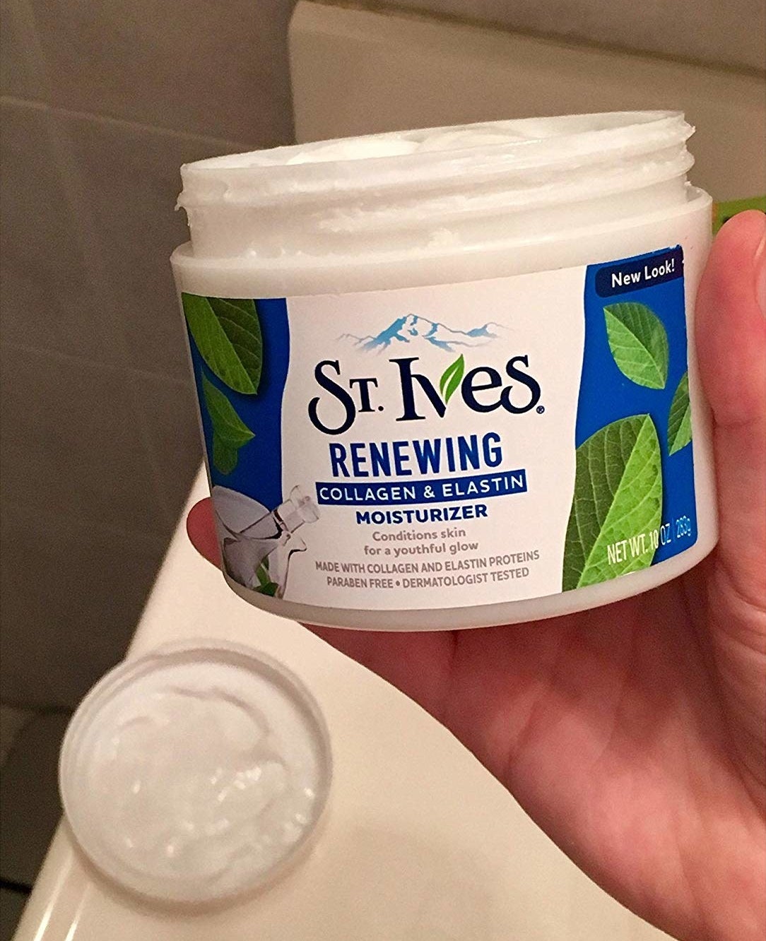 reviewer holding big tub of white moisturizer