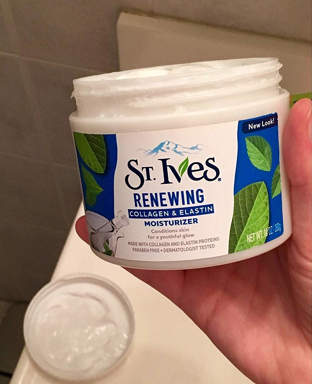 reviewer holding big tub of white moisturizer
