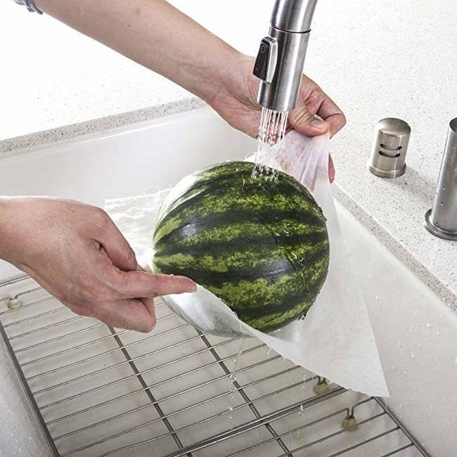 Model's hands holding a bamboo towel sheet under a watermelon while cleaning it