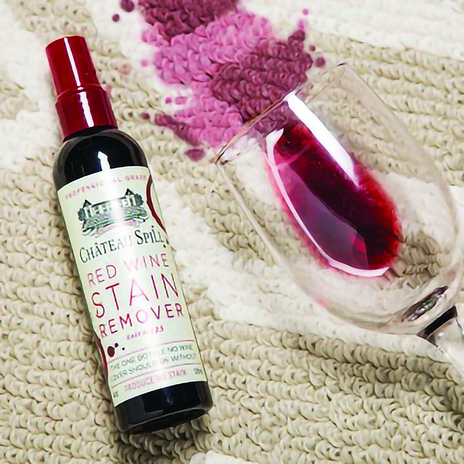 The bottle of red wine stain remover sitting on the carpet next to a spilled red wine glass