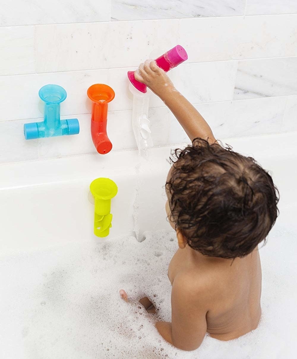 A child pouring water through the tubes attached to the wall of the bathtub 