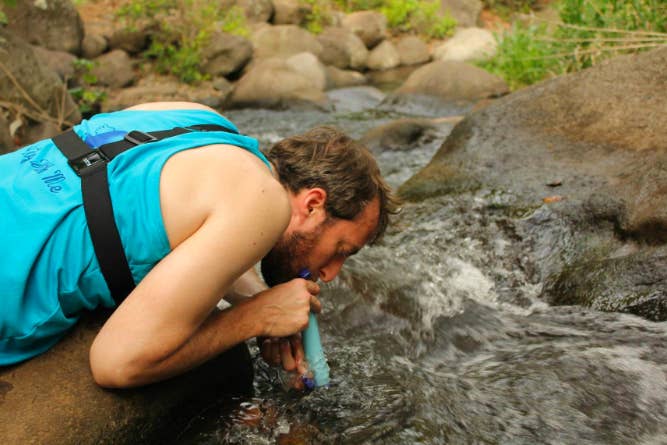 A reviewer holding the LifeStraw to their mouth while taking a drink from a creek