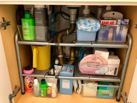 reviewer pic of inside a bathroom vanity cabinet with a lot of organized items in a small space thanks to the adjustable organizer