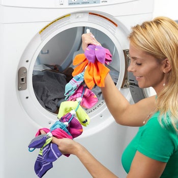 Model holding the long wire SockDock with circles to attach socks, filled with sock pairs next to a washing machine