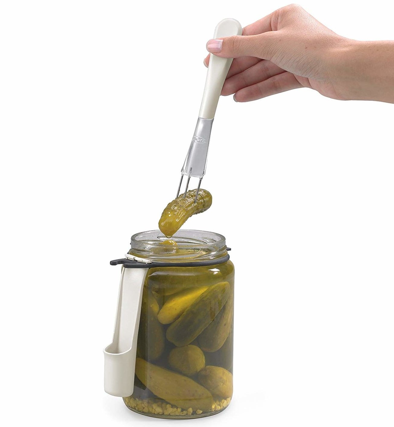 a hand using the condiment fork to take a pickle out of a jar