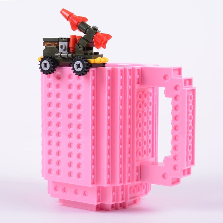 A pink version of the mug with a tiny car on top of the rim