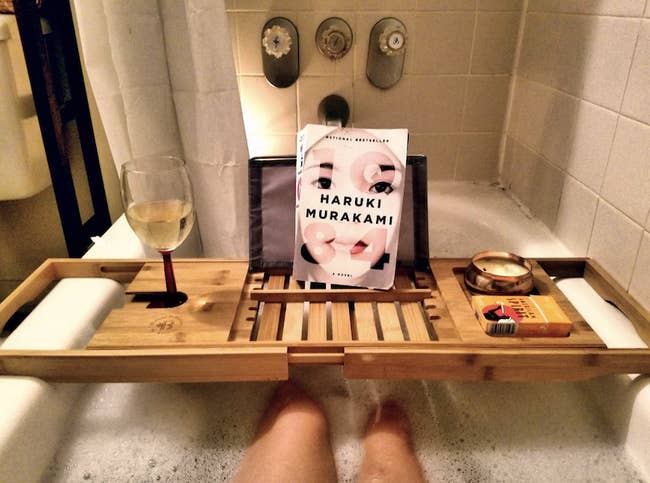 Reviewer's image of long wooden tray that stretches across the entire tub with enough room for their wine, book, and candle to sit on