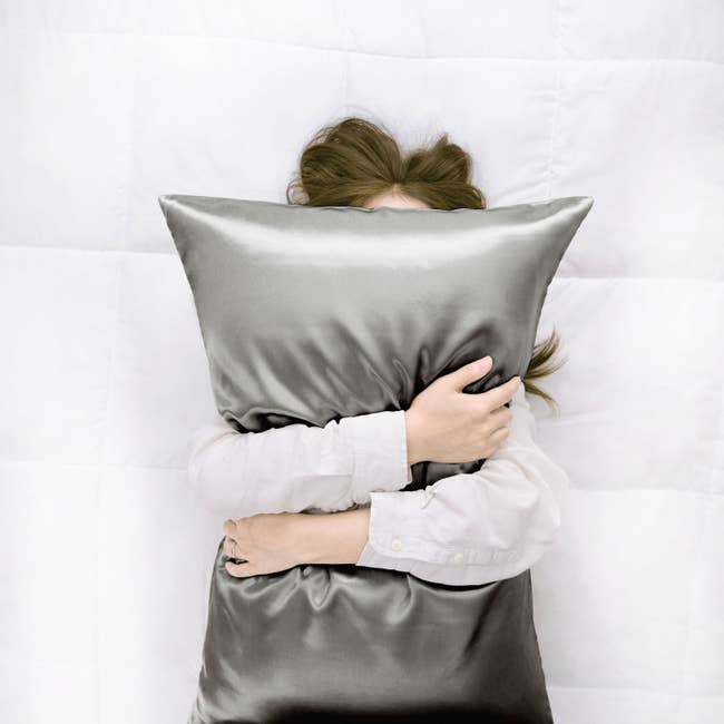 A model clutching a shiny grey satin pillow