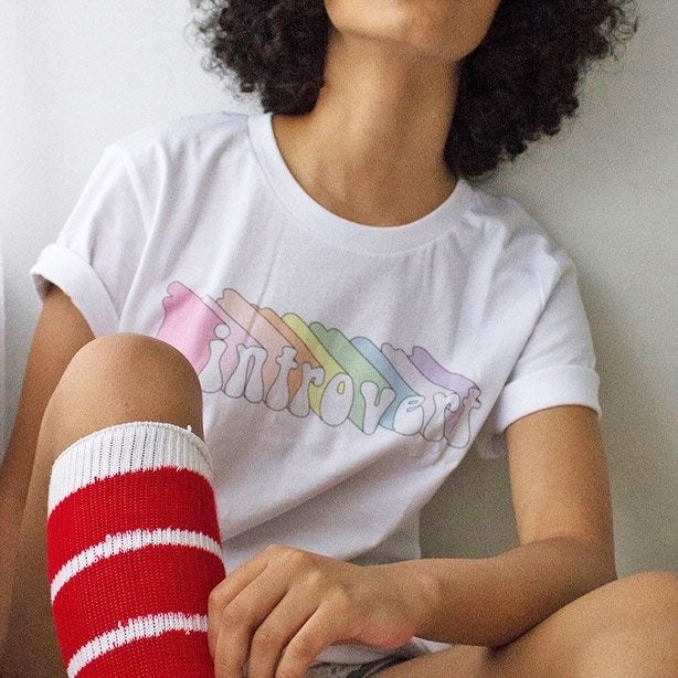 A model wearing a white tee with a graphic illustration of "introvert" in rainbow colors